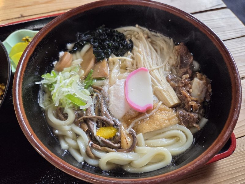 牛肉、お揚げ、たけのこ、えのき、ワカメ、かまぼこ、ネギをのせたしこたまうどん