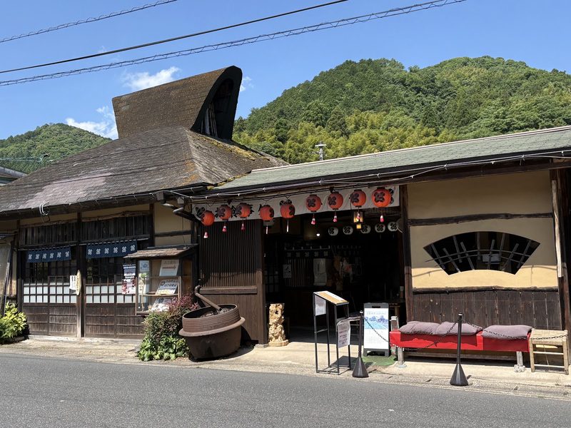 茅葺き屋根風の大きな屋根の下に赤い提灯と扇形の窓が並ぶ、みのやの店構え
